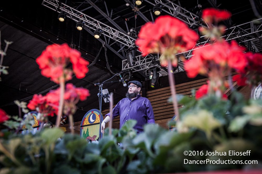 Man on stage with red flowers foreground.