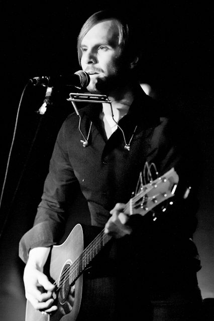 Musician performing with guitar and harmonica.