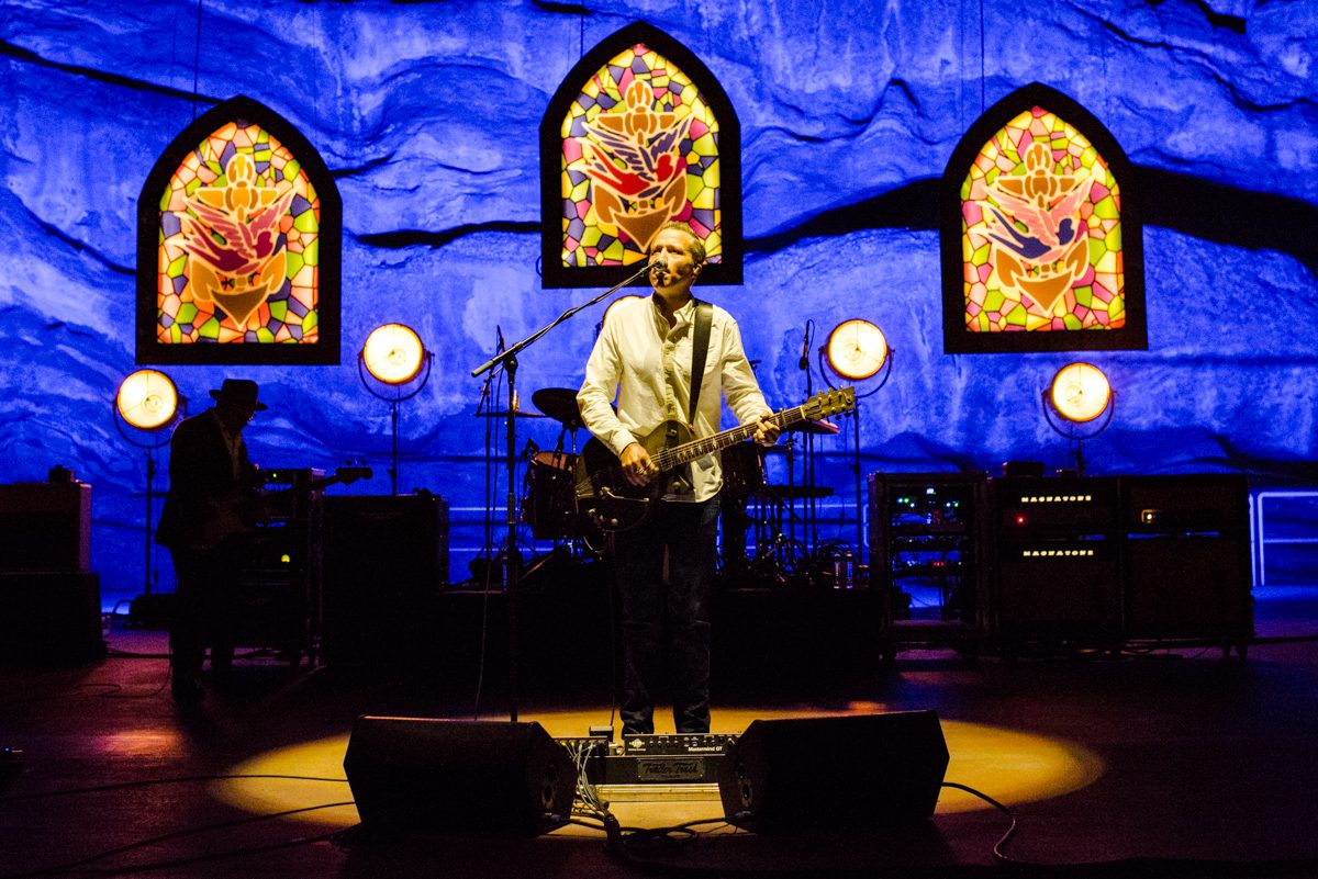 Musician performing on stage with stained glass backdrop.