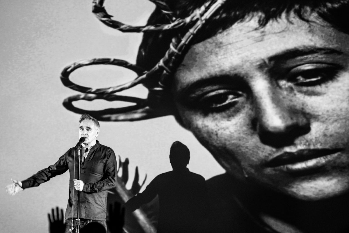 Performer with microphone in front of projection.