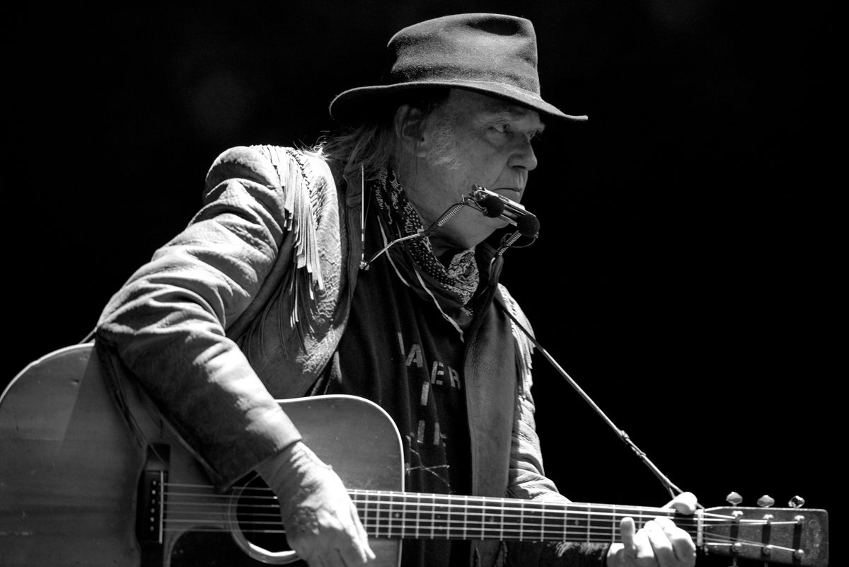 Musician playing guitar with harmonica and hat.