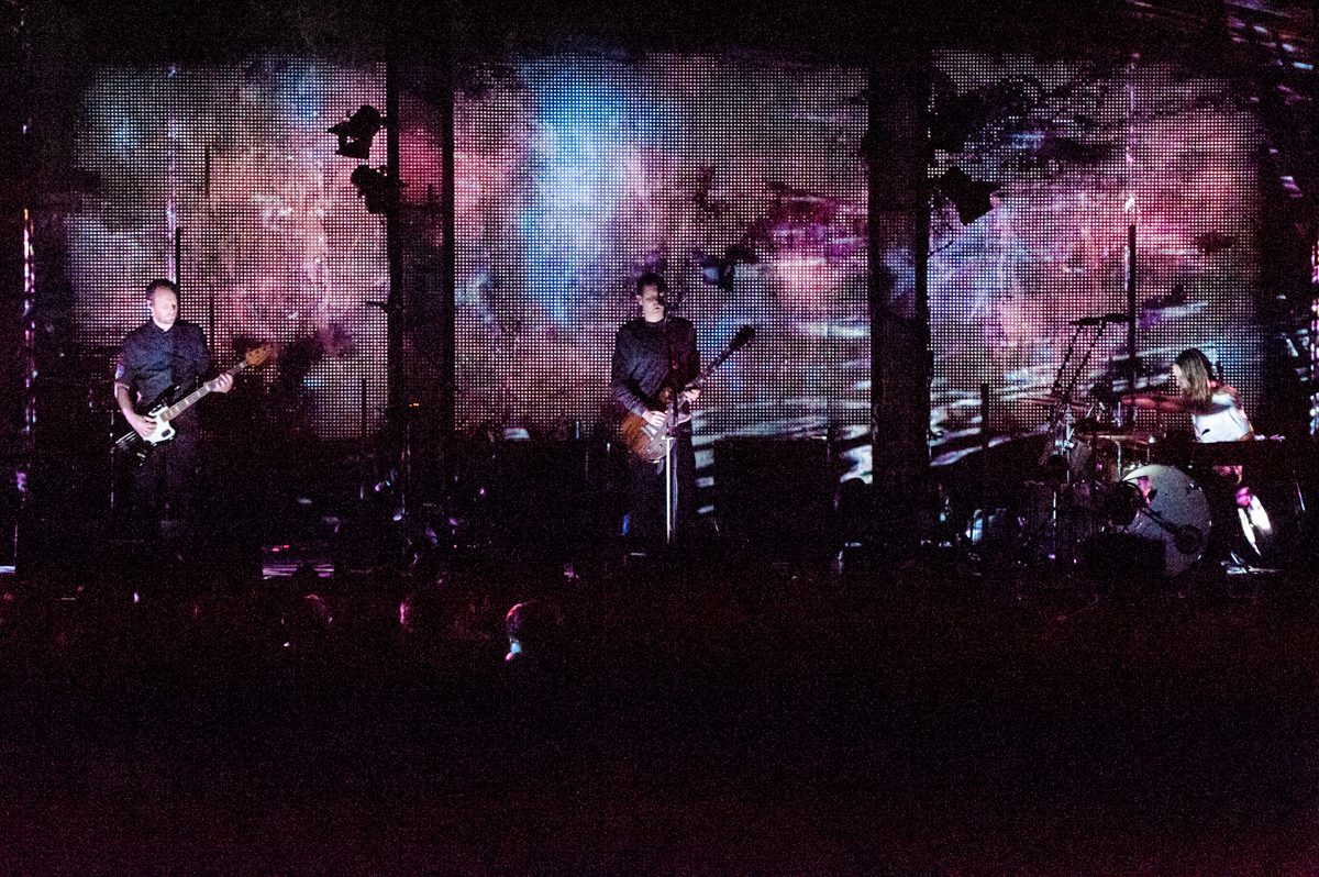 Band performing on stage with colorful backdrop.