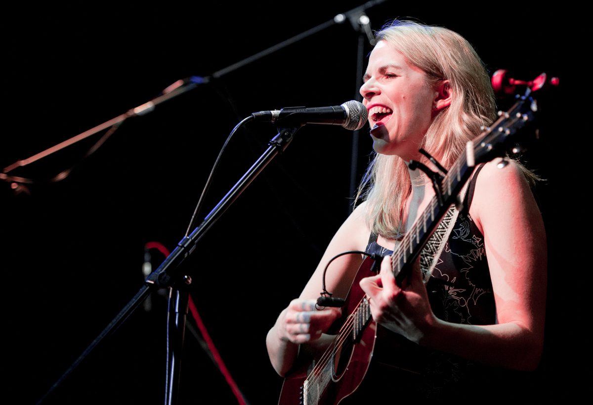 Singer performing with a guitar on stage.