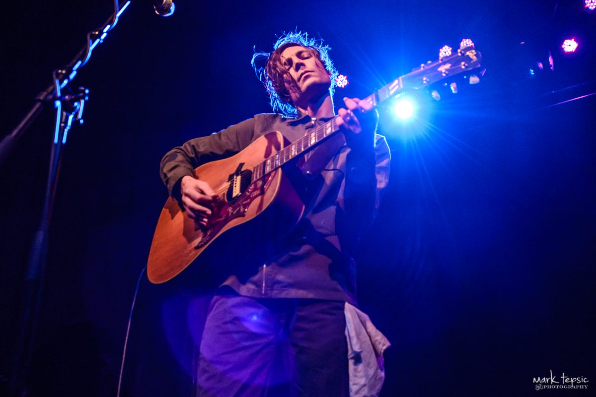 Musician performing with guitar on stage.