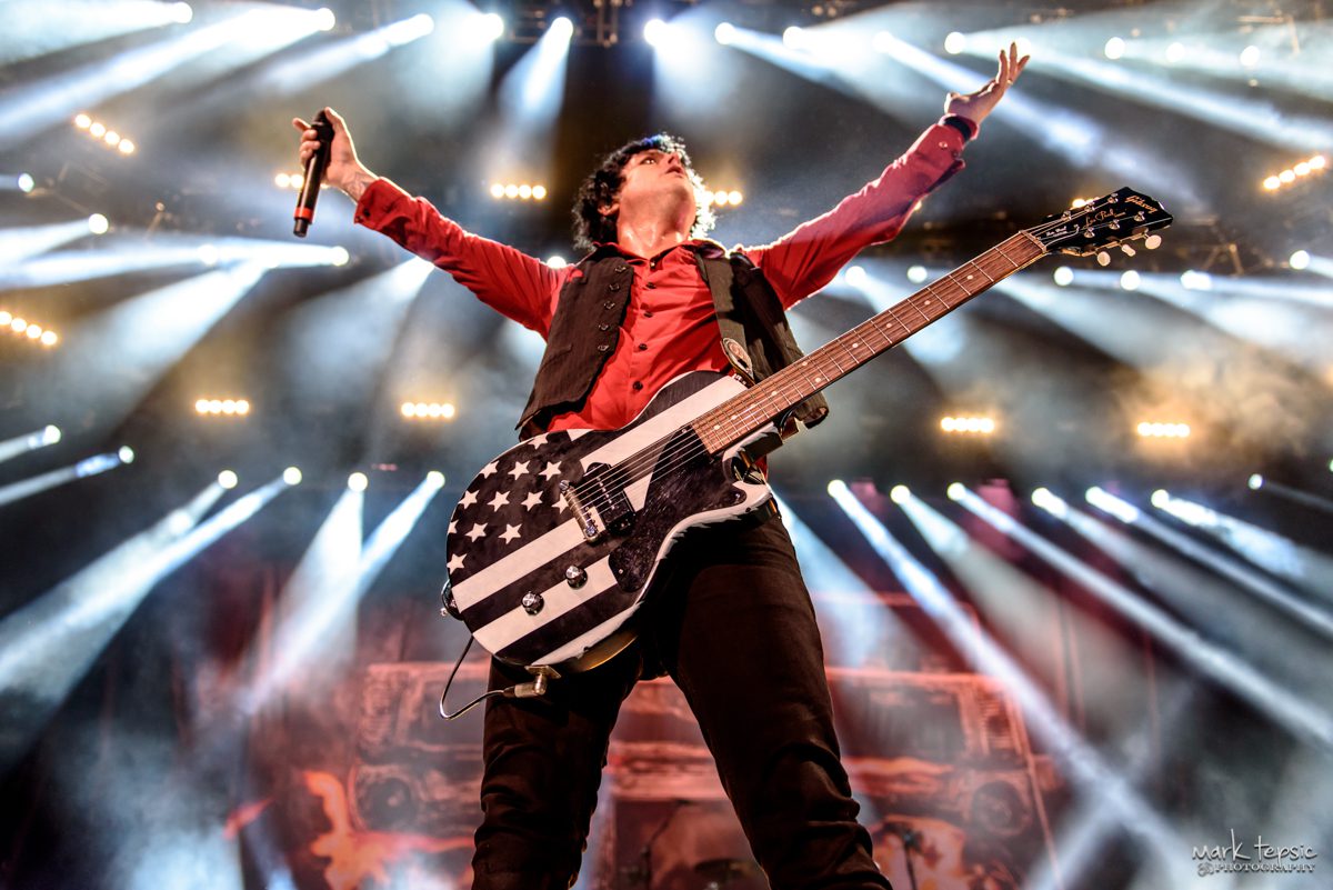 Musician performing energetically with guitar on stage.