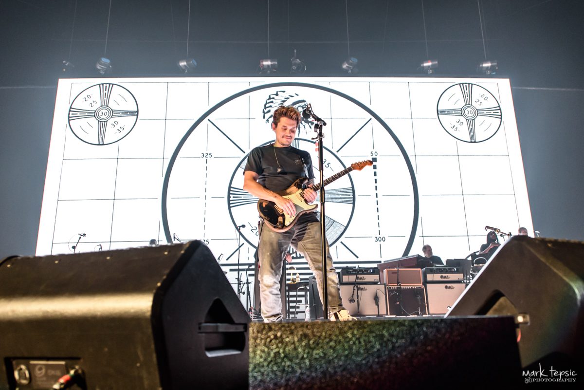 Guitarist performing on stage with visual backdrop.