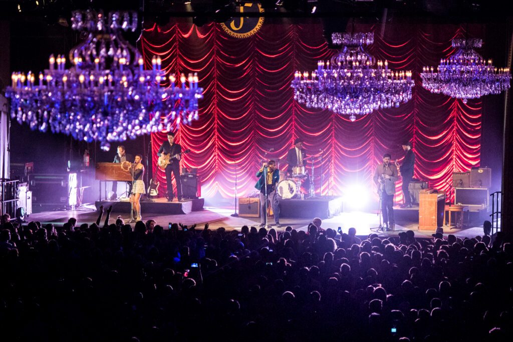 Band performing on stage with chandeliers above.