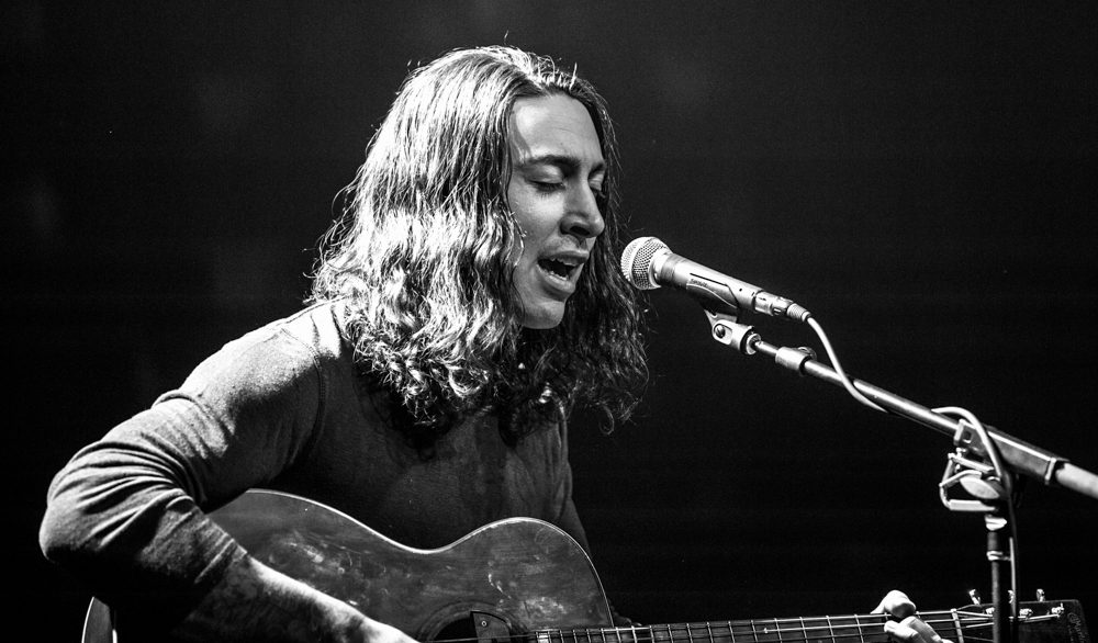 Musician singing and playing guitar on stage.
