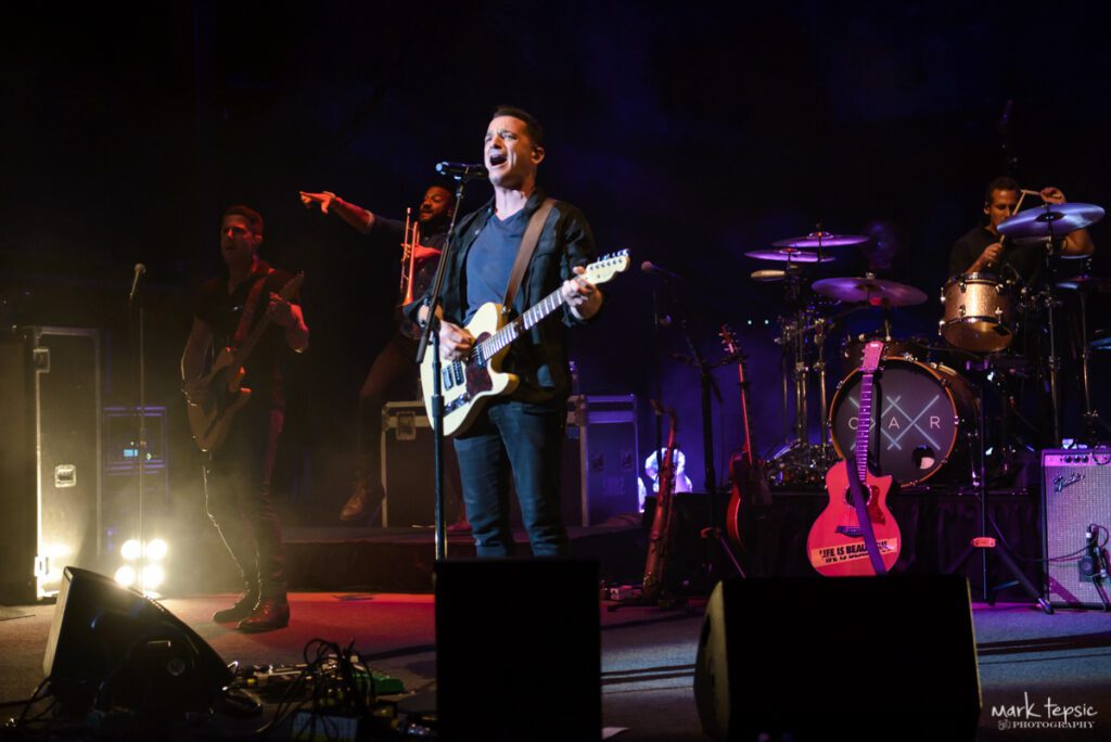 Band performing live on stage with instruments.