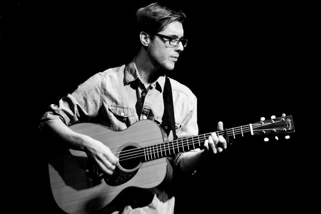 Man playing acoustic guitar in black and white.