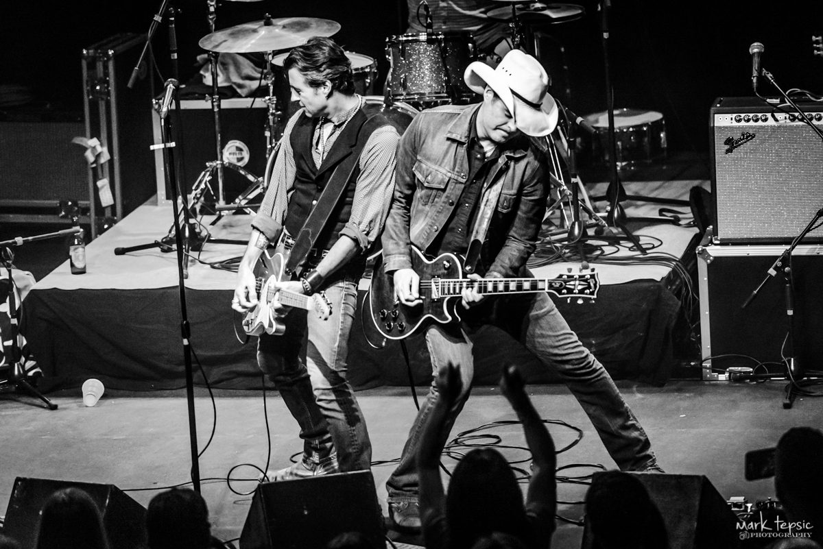 Two guitarists performing energetically on stage.