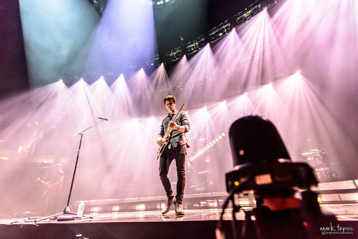 Guitarist performing on stage with dramatic lighting.