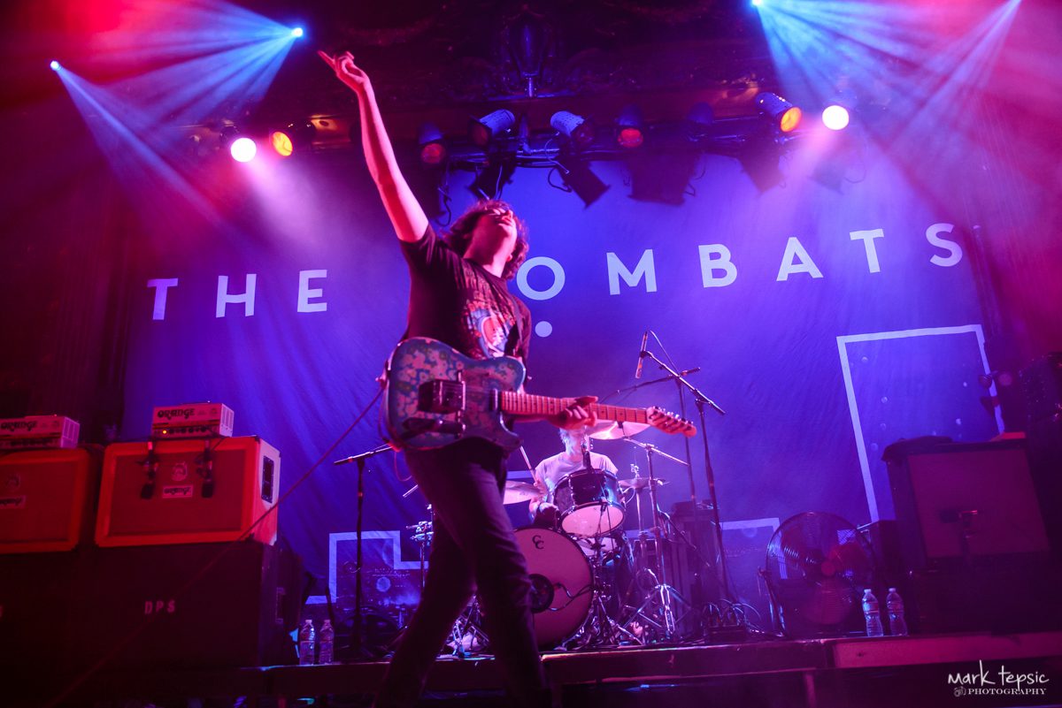 Musician performing energetically on stage with guitar.