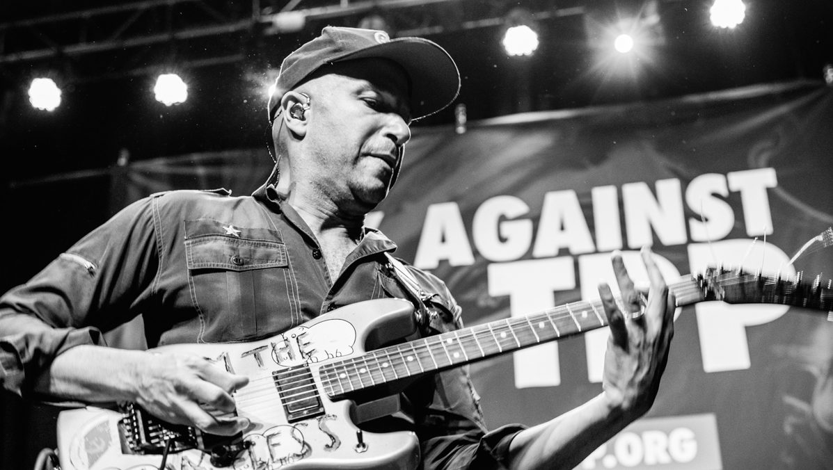 Guitarist performing on stage with banner backdrop.