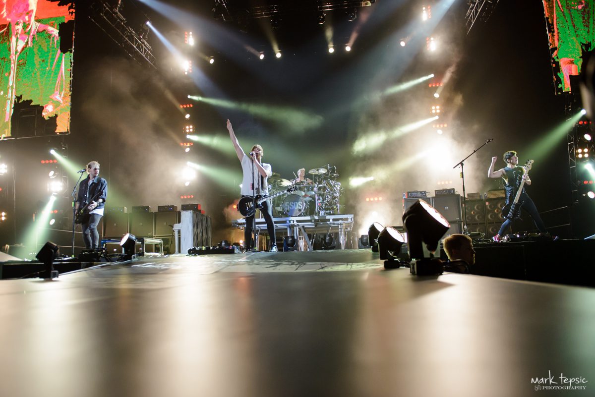 Rock band performing on brightly lit stage.