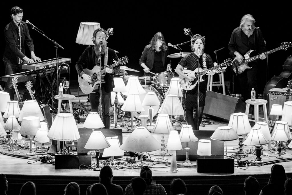 Band performing on stage with many lamps.
