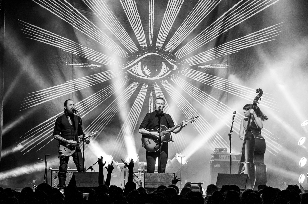 Band performing on stage with eye backdrop.