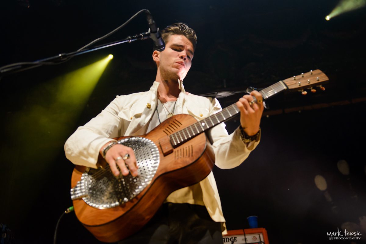 Musician playing guitar on stage under lights.