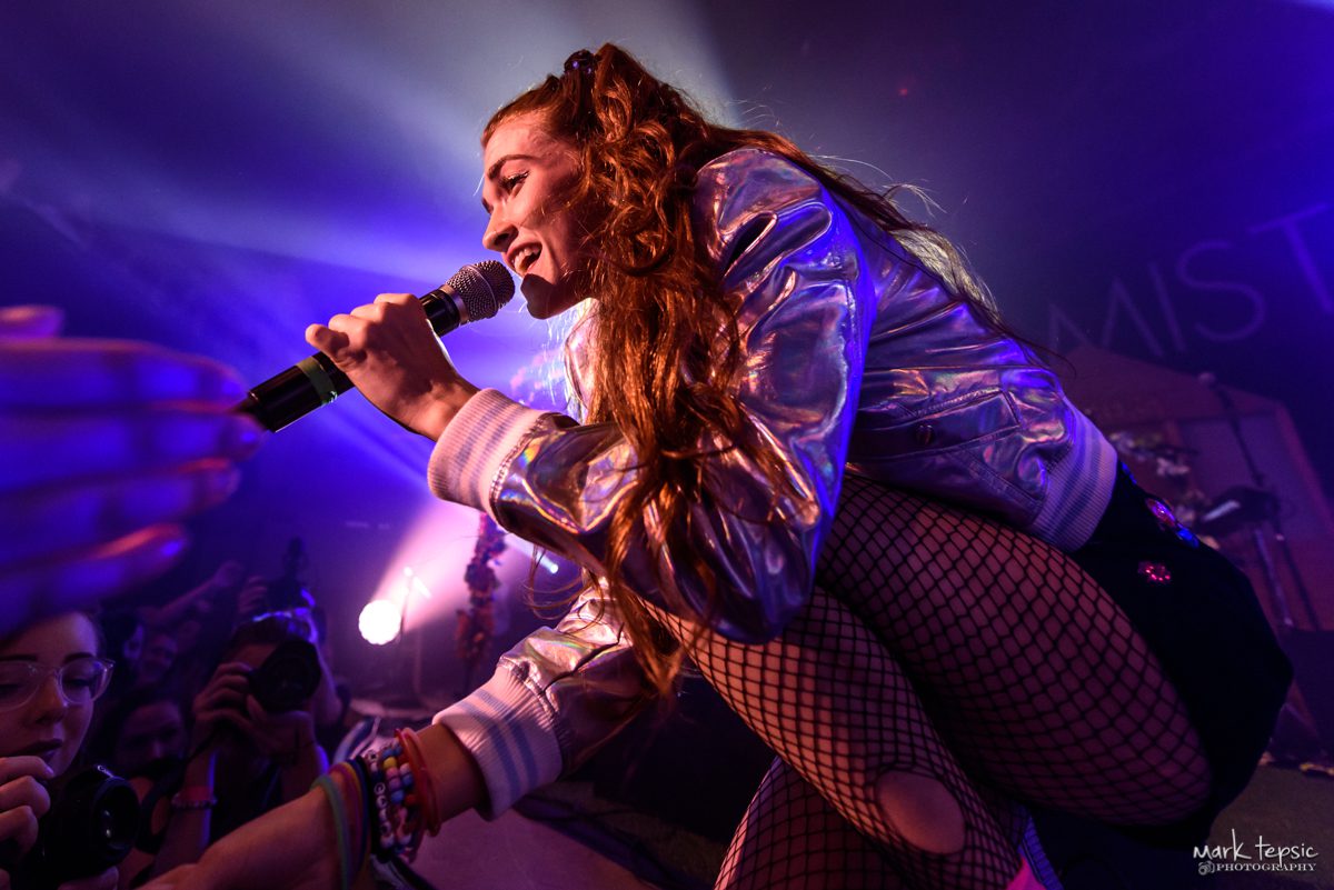 Singer performing energetically on stage with microphone.