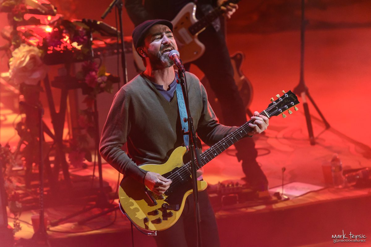 Musician performing on stage with guitar.