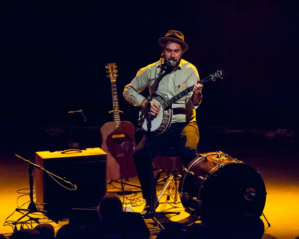 Musician performing on stage with guitar, banjo.