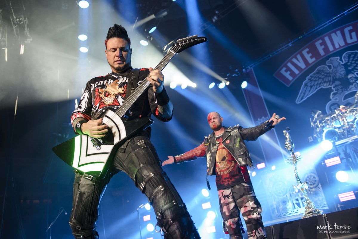 Guitarist performing on stage with band logo.
