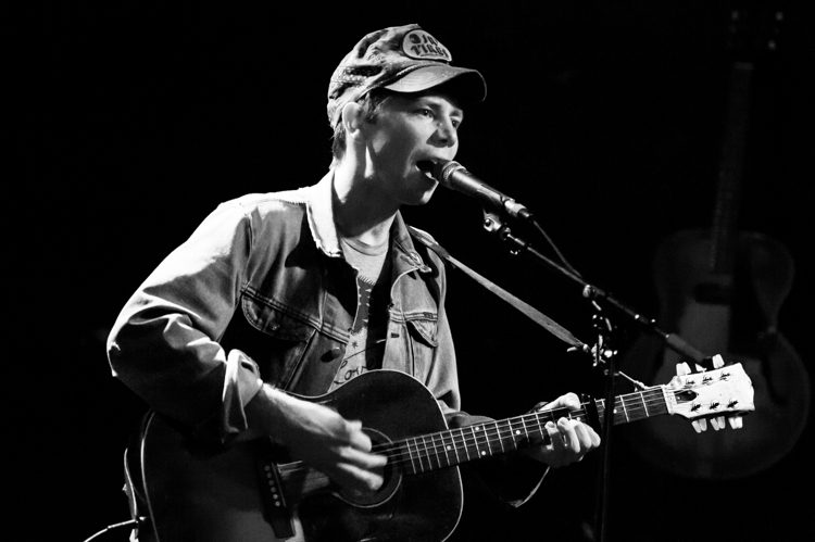 Musician singing and playing guitar on stage.