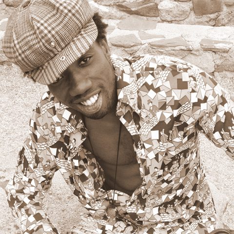 Man smiling in patterned shirt and cap.