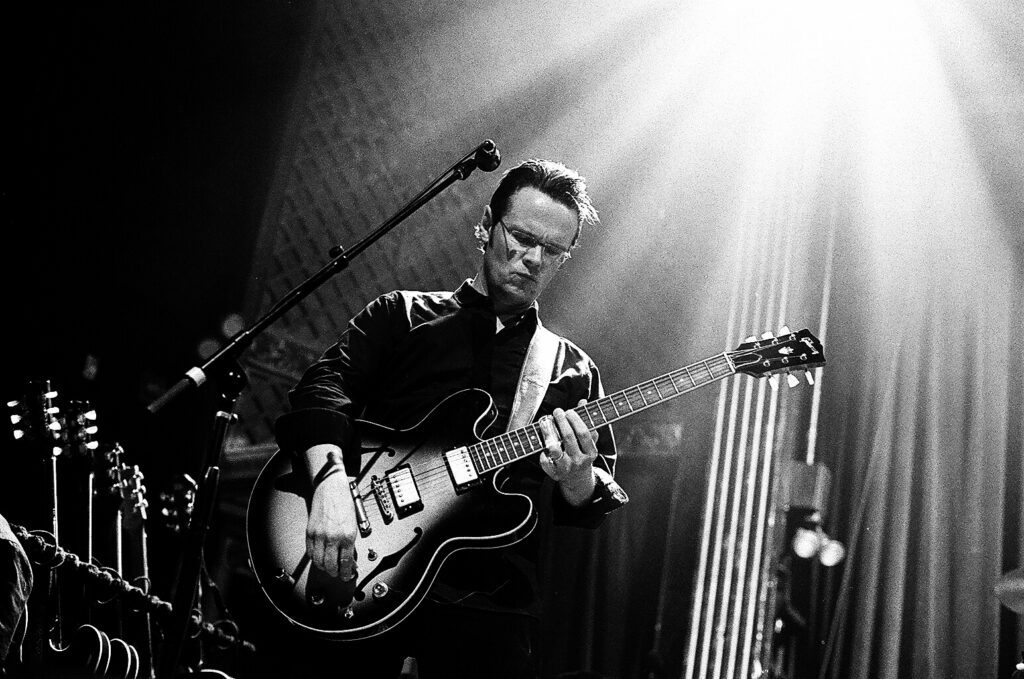 Musician playing guitar on stage, dramatic lighting.