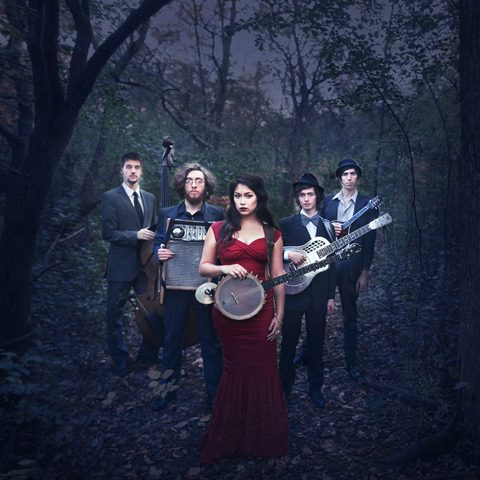 Band posing in forest with instruments.