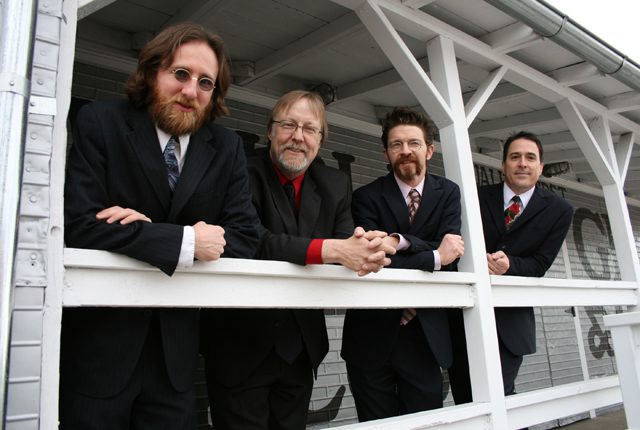 Four men in suits leaning on railing.