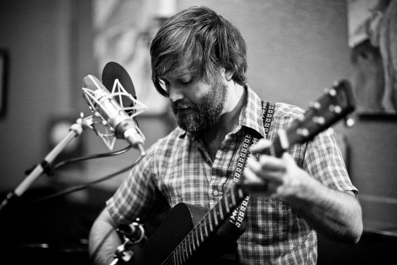 Musician playing guitar near a microphone.