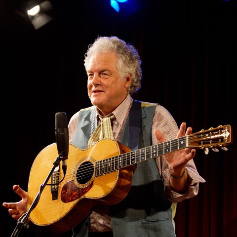 Elderly man playing guitar on stage.