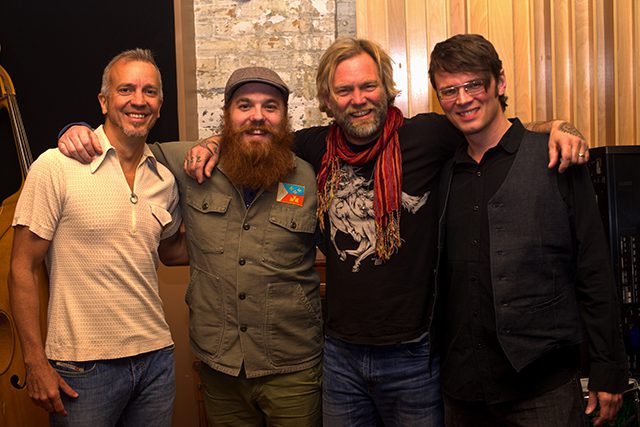 Four smiling men posing in casual attire.