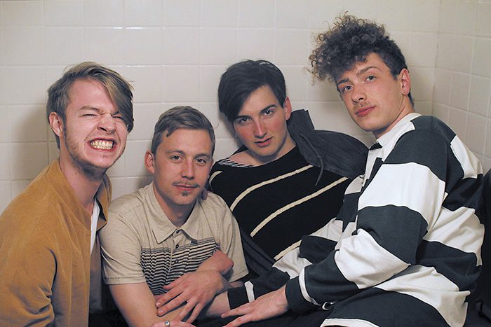 Four men sitting together in a bathroom.