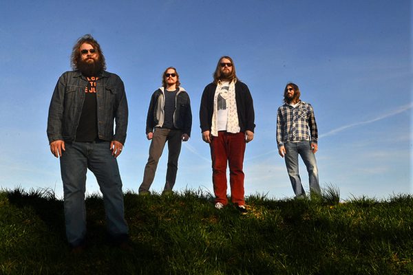 Four men standing on grassy hill.