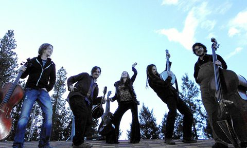 Band posing with instruments under blue sky.