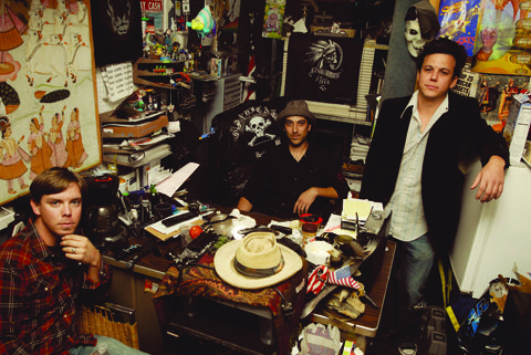 Three men in a cluttered room.