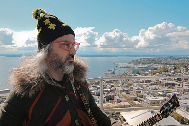 Man with guitar overlooking scenic cityscape.