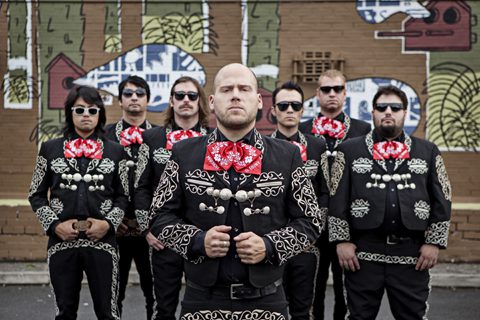 Group in mariachi outfits with mural background.