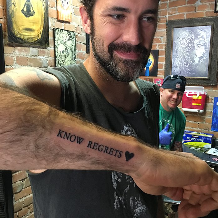 Man showing "Know Regrets" tattoo on arm.