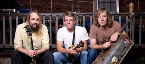 Three men with instruments sitting outside house.