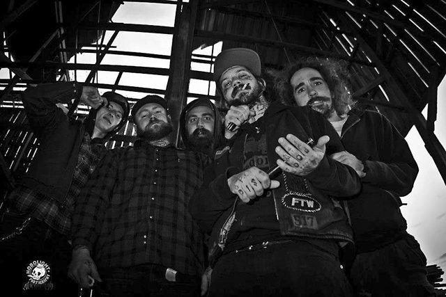 Five men posing under wooden structure, monochrome.