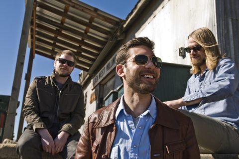 Three men sitting on outdoor steps, smiling.