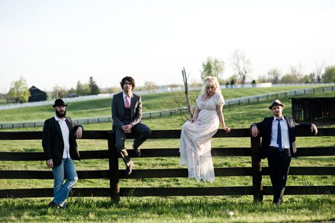 Four people sitting on a wooden fence.