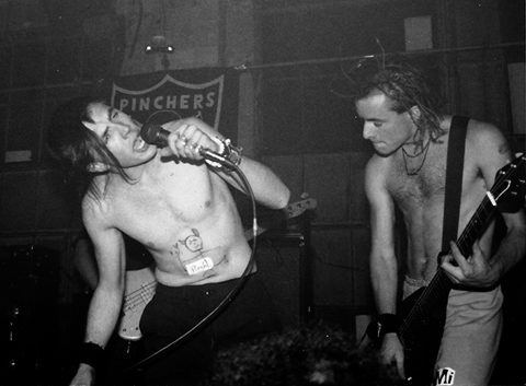 Two shirtless musicians performing energetically on stage.