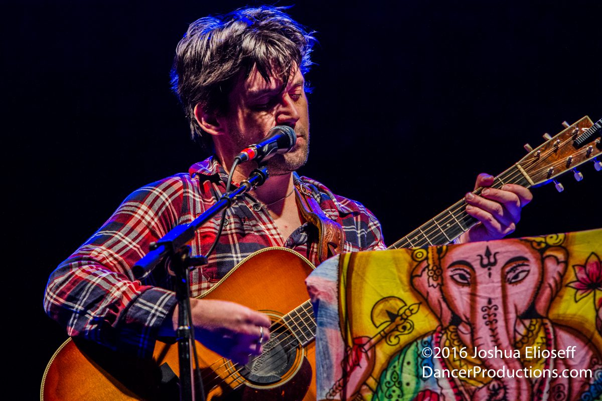 Musician playing guitar on stage, colorful backdrop.