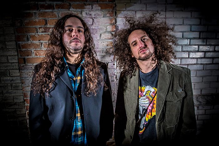 Two men standing against a brick wall.