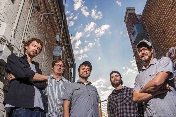 Five men standing in an alleyway, smiling.
