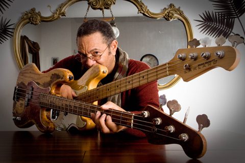 Man holding two electric bass guitars indoors.